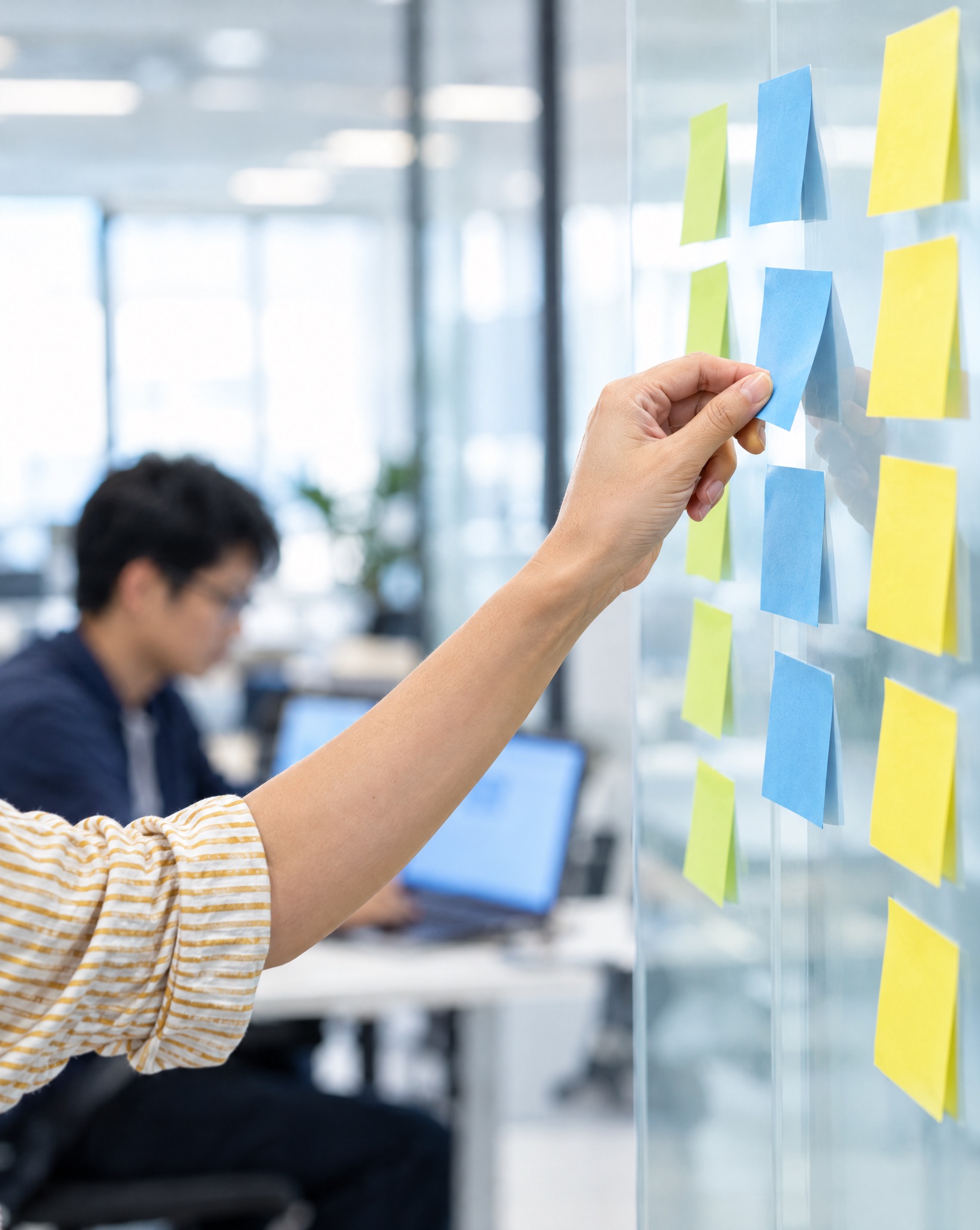 A product owner moving a sticky note into the next column on a glass wall